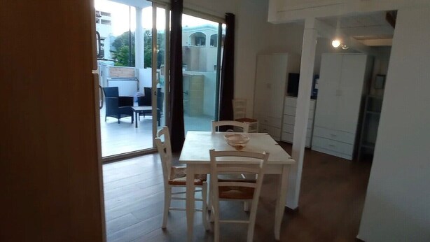 A dining area with a table and chairs, a sliding glass door leading to an outdoor seating area, and a kitchen in the background. - Apartment 'Casa Dell'Oleandro' with Private Terrace, Wi-Fi and Air Conditioning (Olbia)