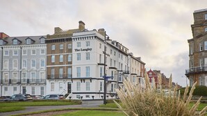 Een historisch gebouw met bord waarop 'The Langley' staat, omringd door andere traditionele gebouwen, een straat en een gazon.