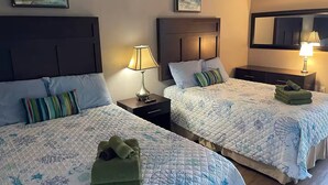 A hotel room with two beds, each with a headboard, a bedside table with a lamp, and a folded green towel on the bed. - Cozy 1-bedroom condo in tranquil Myrtle Beach (Myrtle Beach)