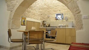 A stone archway leading to a kitchen with wooden cabinets, a dining table with chairs, and a tiled backsplash.