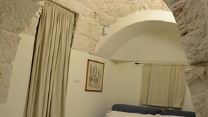 A room with a stone archway, a bed with white bedding, a tray with cups and a bottle, and a framed picture on the wall.