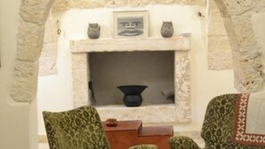 A stone-walled room with a fireplace, two patterned armchairs, a round table, and a pitcher on the table.