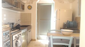 Une cuisine équipée d’une cuisinière, d’un évier et d’un réfrigérateur. On y trouve une table en bois avec des chaises et un saladier.