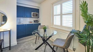 A modern kitchen with blue cabinets, a glass dining table, and a large window with blinds. - Host & Stay | The Langley Hotel, Apartment 8 (Whitby)