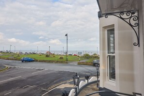 Eine Küstenstraße mit einem blauen Auto, einem weißen Gebäude mit einem Fenster und einer Straßenlaterne.