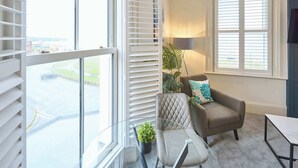 Ein modernes Wohnzimmer mit einem großen Fenster, einer Couch, einem Glastisch und einem Blumentopf.