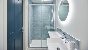 Ein modernes Badezimmer mit einer Duschkabine aus Glas, einem weißen Waschbecken und einem runden Spiegel.