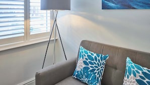 Un soggiorno con un divano grigio, due cuscini decorati, una lampada da terra e un quadro appeso al muro.