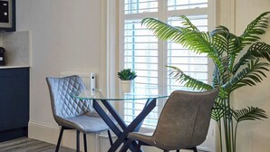 Ein Essbereich mit einem Glastisch, zwei Stühlen, einem Blumentopf und einem Fenster mit Jalousien.