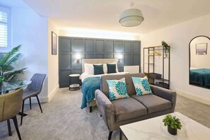 Ein modernes Schlafzimmer mit einem großen Bett, einem Sofa, einem kleinen Tisch und einem Sessel. Auf dem Tisch steht eine Pflanze und an der Wand hängt eine Hängepflanze.