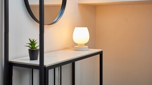 Una mesita de noche con una lámpara, una planta pequeña en maceta y un espejo en la pared.
