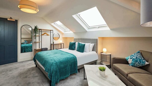 Un dormitorio moderno con tragaluces, una cama con ropa de cama color turquesa, un sofá y una mesita de centro.