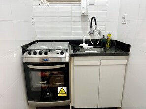Uma cozinha compacta com fogão a gás, forno e pia com torneira.