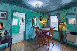 A room with a green door, a round table with chairs, a chandelier, and a mirror on the wall.