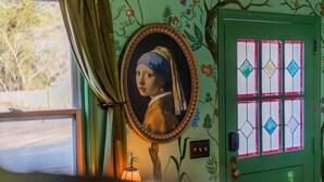 Une pièce avec une porte verte, un miroir orné d’un tableau encadré et une fenêtre avec des rideaux.