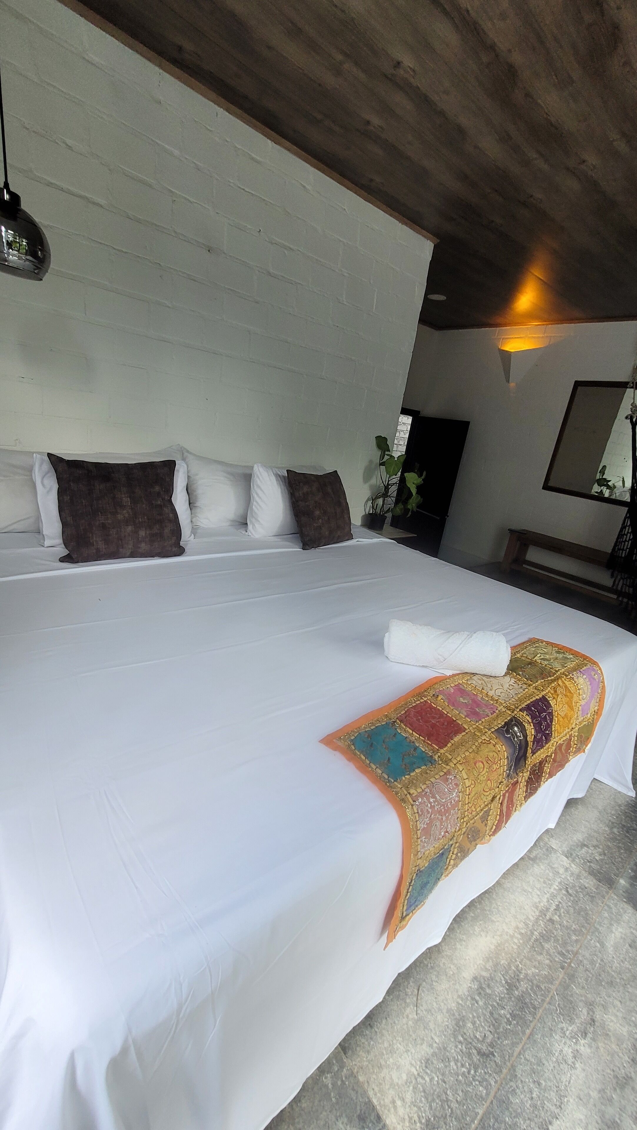 A large bed with white linens, a colorful blanket, and several pillows.