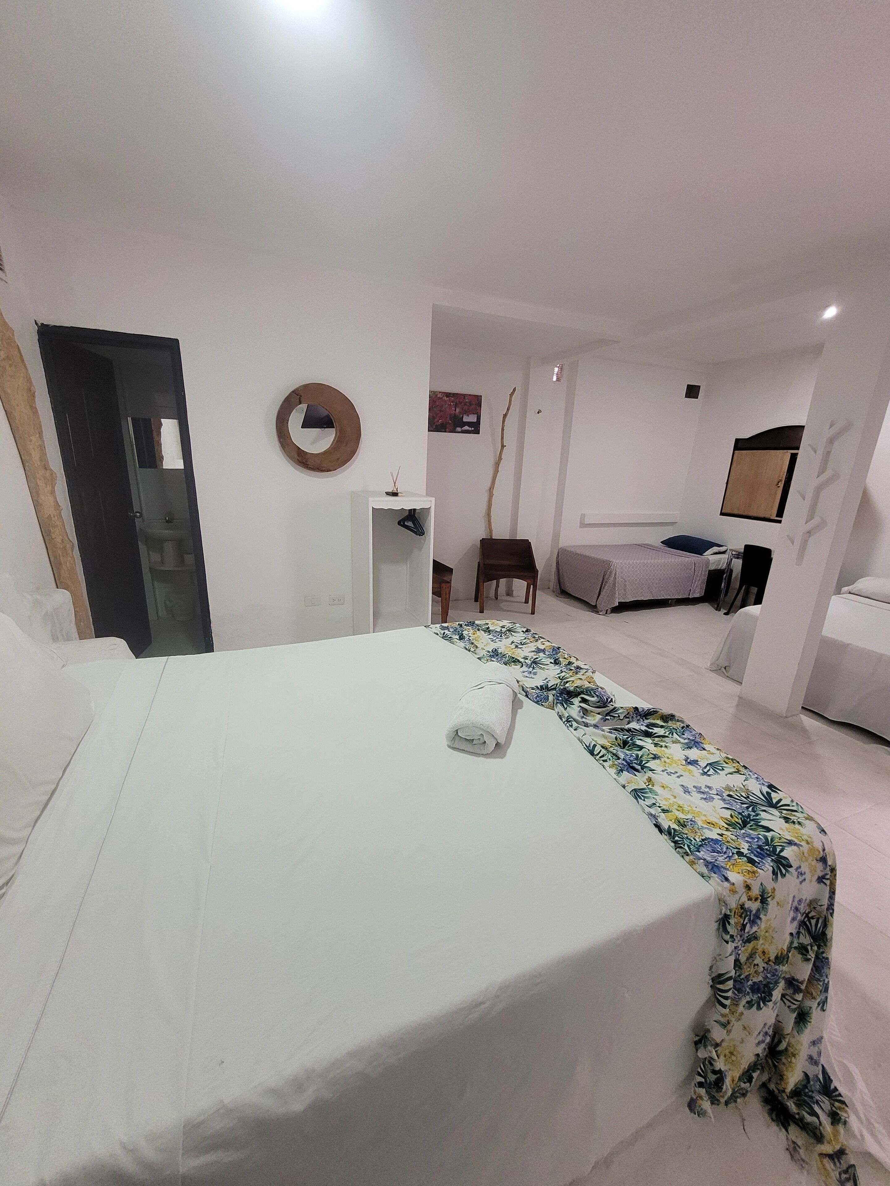 A hotel room with a large bed, a small desk, a chair, a wardrobe, and a bathroom visible through an open door.