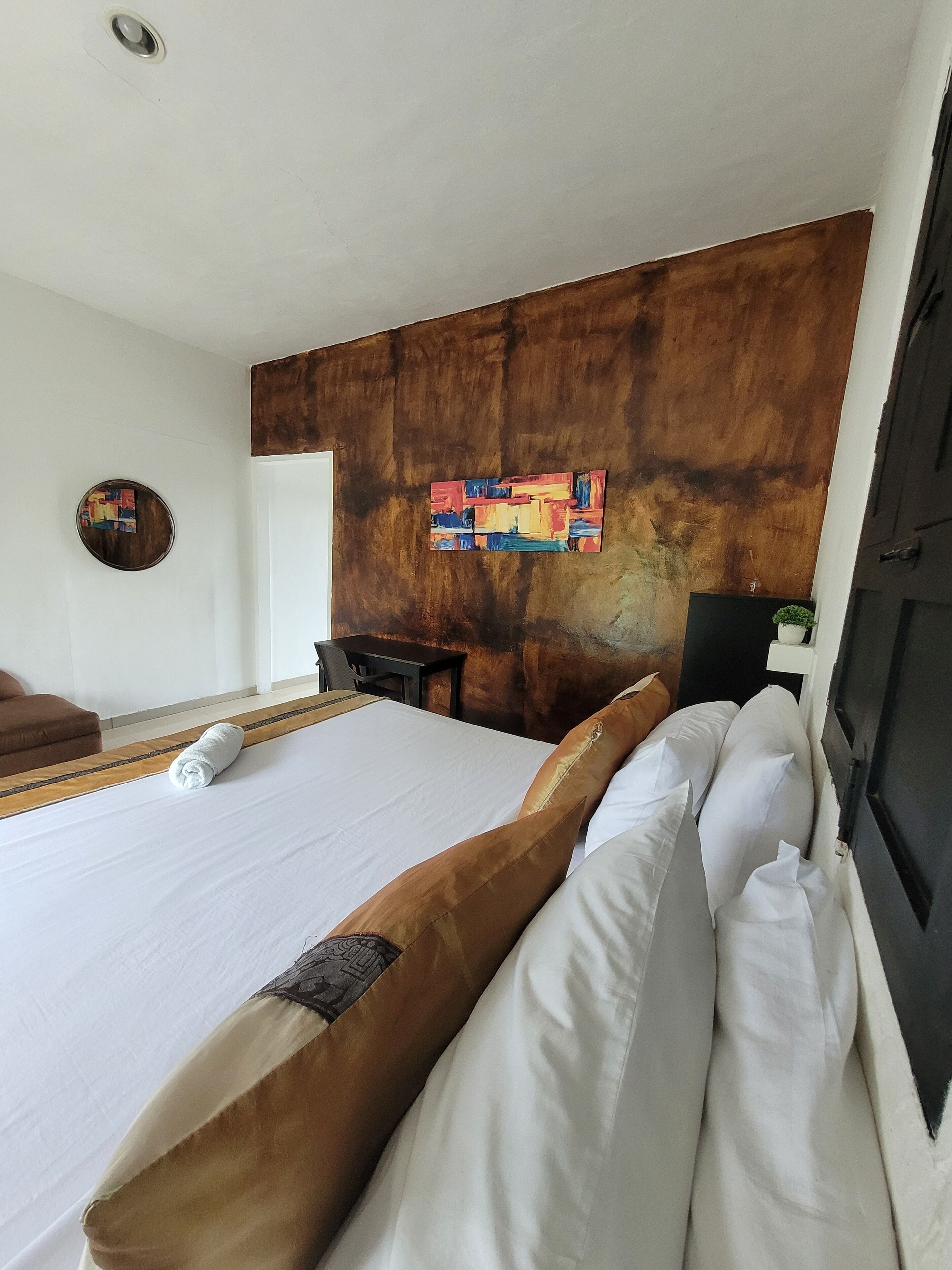 A hotel room with a large bed, a wooden accent wall, a small table, and a chair.
