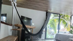 Ein geräumiges Zimmer mit einer Hängematte, einem Bett, einem Fernseher und Blick ins Grüne.