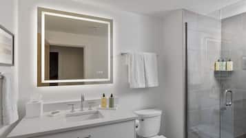A modern bathroom with a white sink, a toilet, a glass shower enclosure, and a large mirror with integrated lighting.