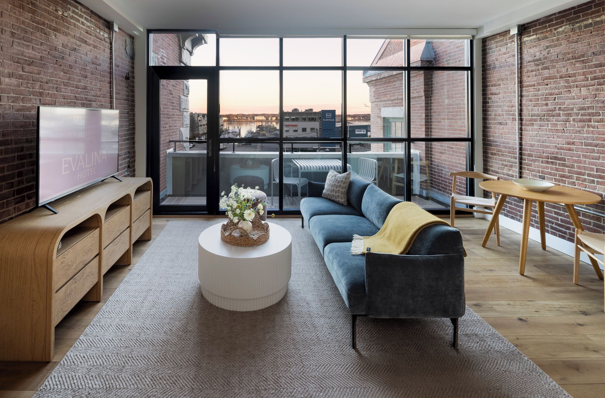 Una sala de estar moderna con un sofá, una mesa de centro, un televisor y vistas de la ciudad a través de amplios ventanales.