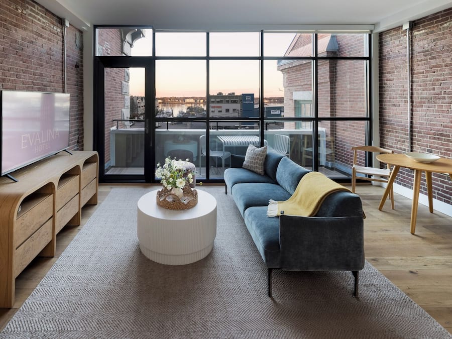 Una sala de estar moderna con un sofá, una mesa de centro, un televisor y vistas de la ciudad a través de amplios ventanales.