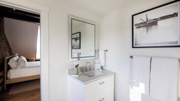 A hotel room with a bed, a bathroom with a sink, mirror, and a framed picture on the wall.