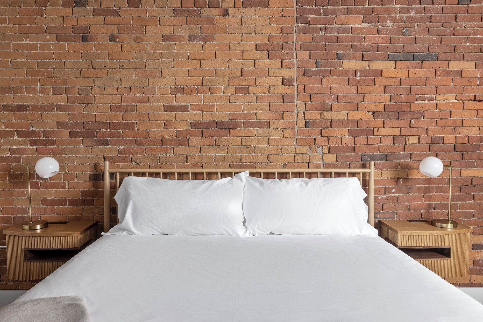 A bed with white bedding, two bedside tables with lamps, and a brick wall background.