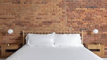 A bed with white bedding, two bedside tables with lamps, and a brick wall background.