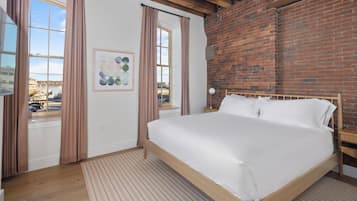 A bedroom with a wooden bed, a brick wall, and a window with curtains.