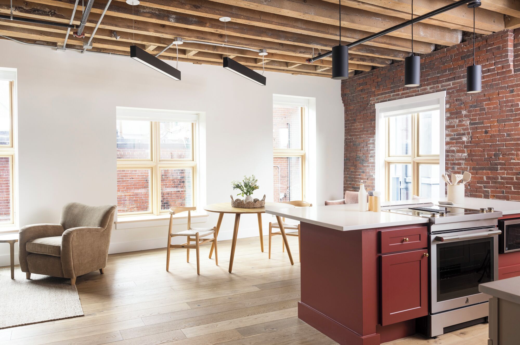 A modern kitchen with a red island, wooden beams, and large windows.