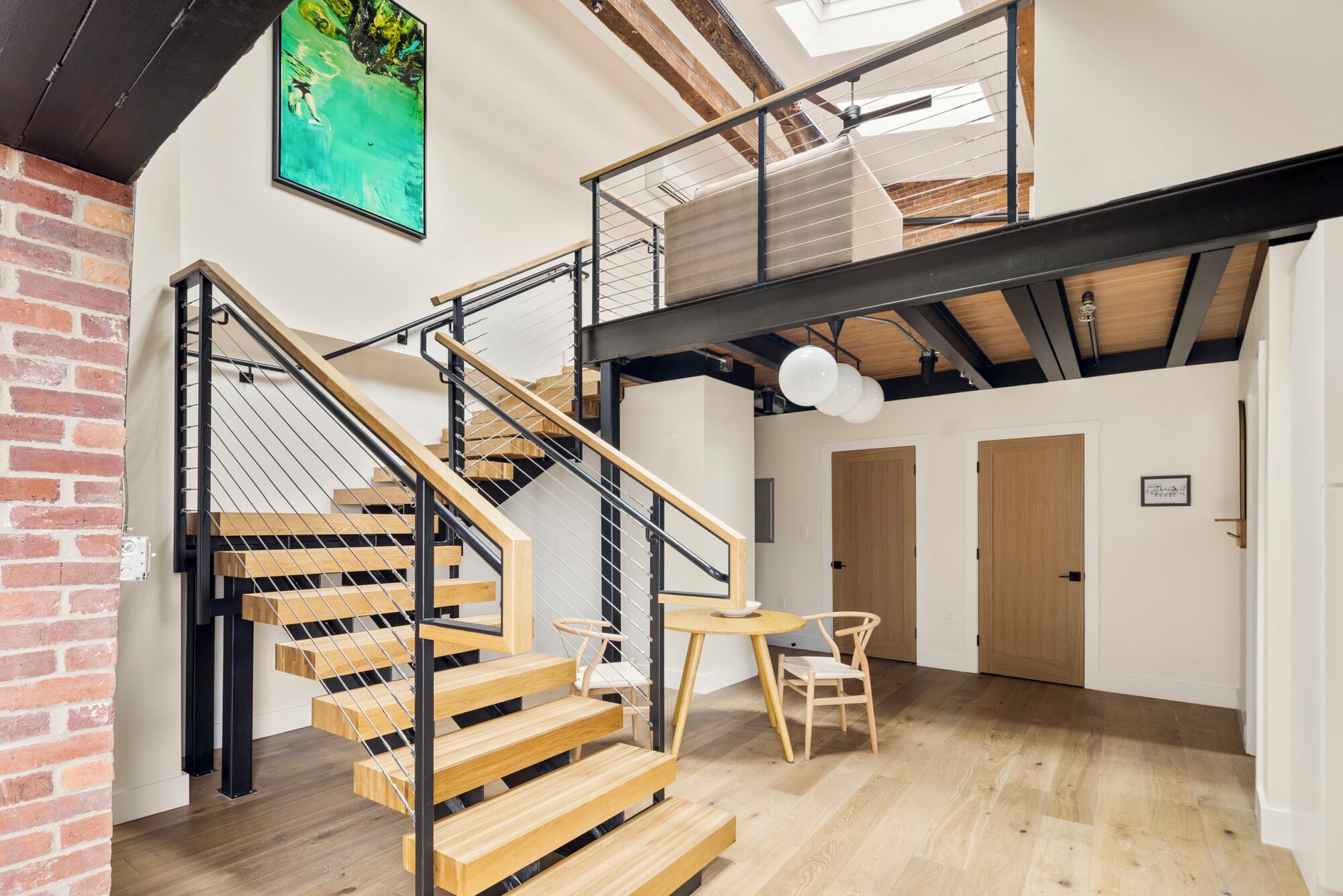 A multi-level interior with a wooden staircase, a dining area, and a view of the sky through a skylight.