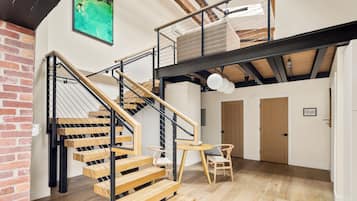 Un interior de varios niveles con una escalera de madera, un comedor y vistas del cielo a través de un tragaluz.