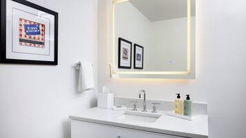 A modern bathroom with a white vanity, a large mirror with underglow lighting, and two framed pictures on the wall.