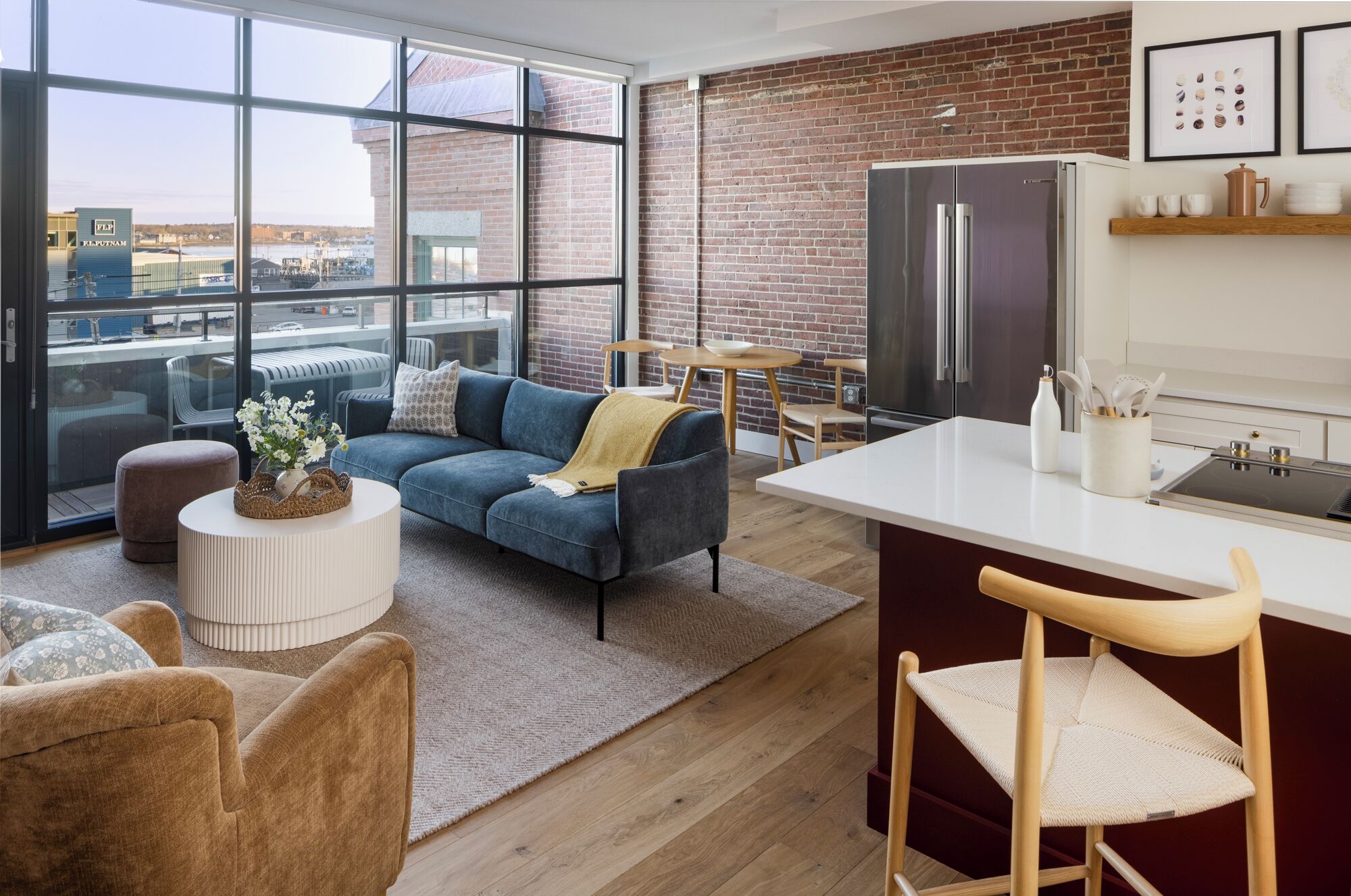 A modern apartment with a large window, a blue sofa, a kitchen with a refrigerator, and a dining area.