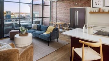A modern apartment with a large window, a blue sofa, a kitchen with a refrigerator, and a dining area.