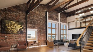 A spacious living area with exposed brick walls, a wooden staircase, and a large window offering a view of the city. - Evalina Hotel (Portland)