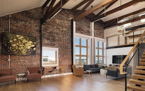 A spacious living area with exposed brick walls, a wooden staircase, and a large window offering a view of the city.
