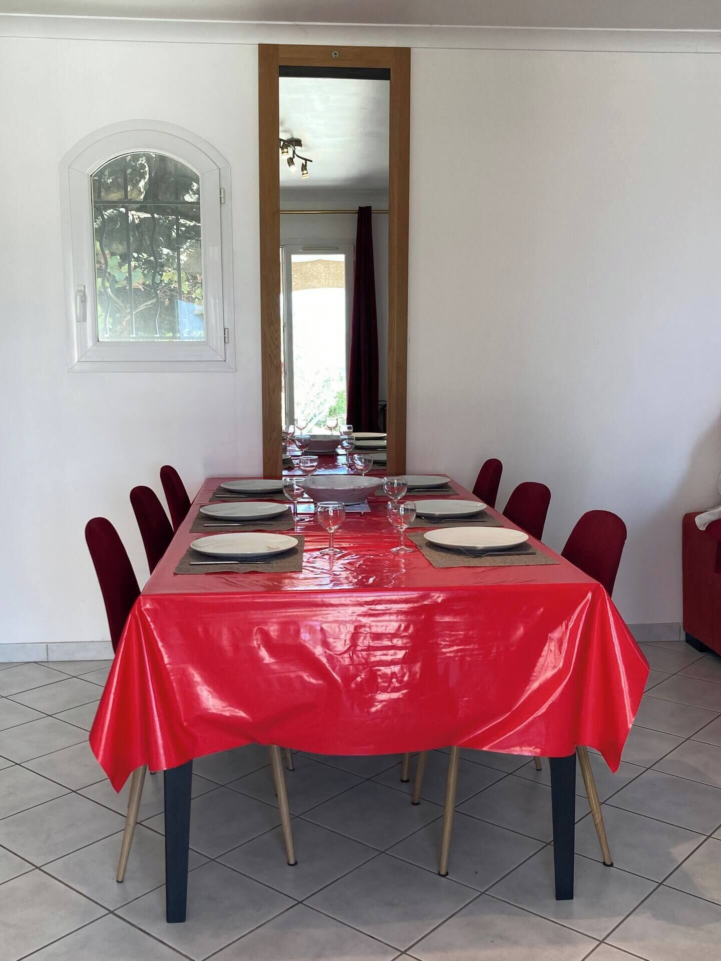 Une salle à manger avec une table rouge dressée pour six personnes, des assiettes blanches et des chaises rouges.