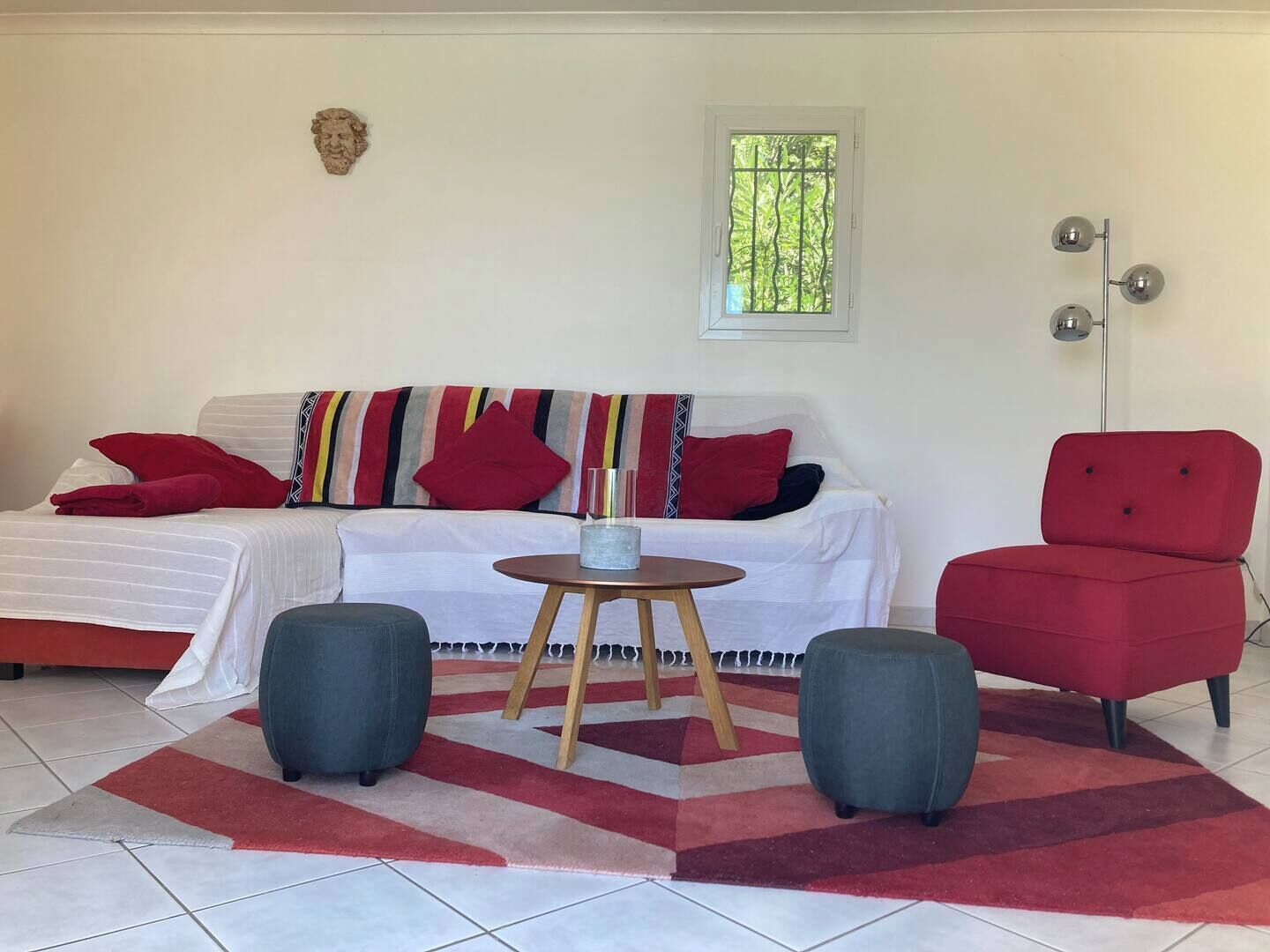 Un salon comprenant un canapé, deux poufs, une petite table ronde et un fauteuil rouge.