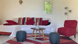 En stue med sofa, to fodskamler, et lille rundt bord og en rød lænestol.