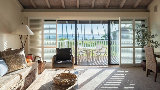A cozy living room with a sofa, a chair, a table, and a view of the ocean through large sliding doors. - 2 Story Ocean-View 2BR, 2 Lanais, Vaulted Ceilings, Resort Pool -Unit 23 (Koloa)