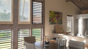 A dining area with a large table, wicker chairs, and a view through large windows. - 2 Story Ocean-View 2BR, 2 Lanais, Vaulted Ceilings, Resort Pool -Unit 23 (Koloa)