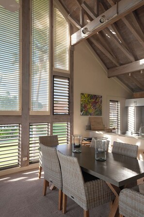 A dining area with a large table, wicker chairs, and a view through large windows. - 2 Story Ocean-View 2BR, 2 Lanais, Vaulted Ceilings, Resort Pool -Unit 23 (Koloa)