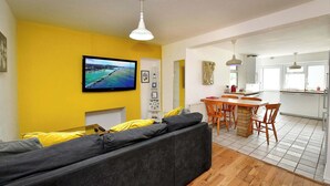 Una sala de estar con sofá, televisión y comedor con mesa y sillas.
