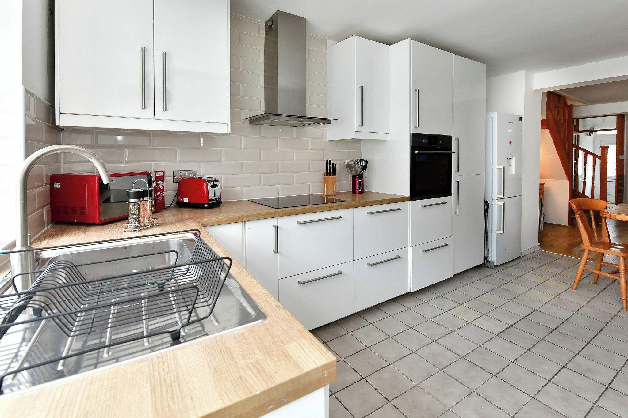 A modern kitchen with white cabinets, a stainless steel range hood, a red toaster, and a built-in oven.