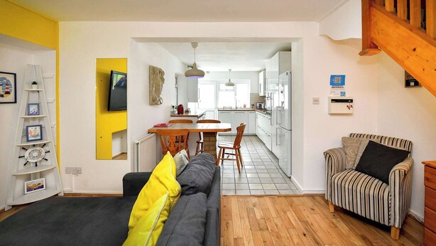 Un espacio habitable compacto con sofá, un sillón a rayas, una mesa de comedor y una zona de cocina.