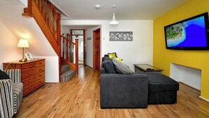 Una sala moderna con una escalera de madera, un sofá seccional gris, un aparador de madera y un televisor de pantalla plana montado en una pared amarilla.