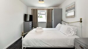 Habitación de hotel con cama, televisor, armario y ventana con cortinas.