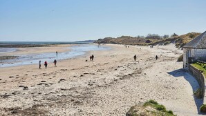 En sandstrand med folk som promenerar och en byggnad med ett välvt tak.